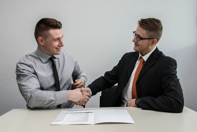 Dois homens sorrindo e apertando as mãos em um escritório, fechando um acordo
