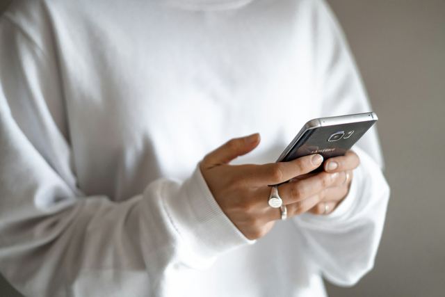 Mulher de blusa branca olhando o celular que segura nas mãos