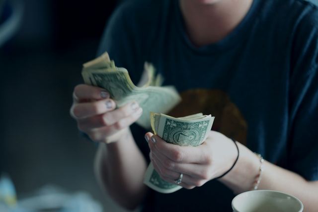 Mulher contando notas de dólar nas mãos, com o foco nas cédulas