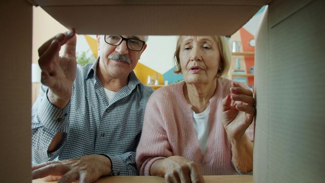Casal de idosos sorrindo enquanto abre uma caixa de papelão recém-entregue