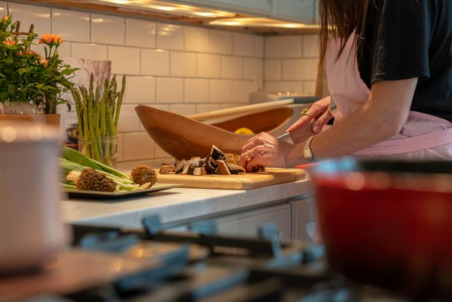 Mulher numa cozinha cortando legumes numa tábua para preparar uma refeição