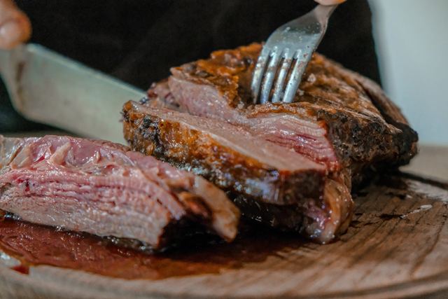 Homem fatiando uma peça de carne assada sobre uma tábua de madeira
