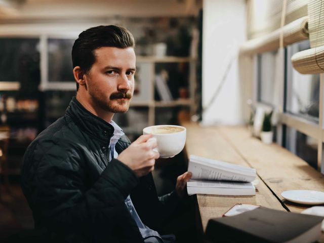 Homem de jaqueta preta segurando uma caneca branca de café.