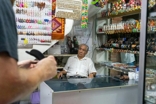 Lojista de camisa branca em pé diante do balcão da própria loja, com ar cansado depois do expediente