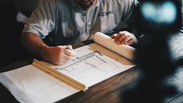 Arquiteto trabalhando num desenho técnico com lápis e régua sobre a mesa