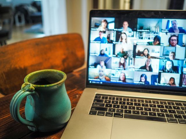 Notebook mostrando uma chamada de vídeo com várias pessoas e uma xícara de café ao lado