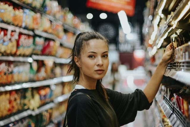 Mulher fazendo compras no corredor de um supermercado, olhando os produtos nas prateleiras