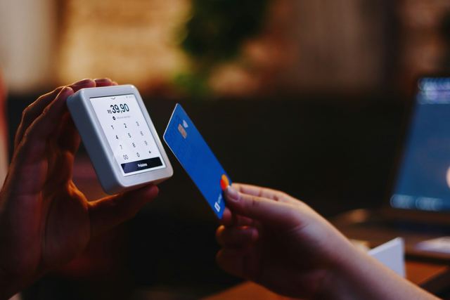 Pessoa segurando um cartão de crédito numa mão e um celular na outra