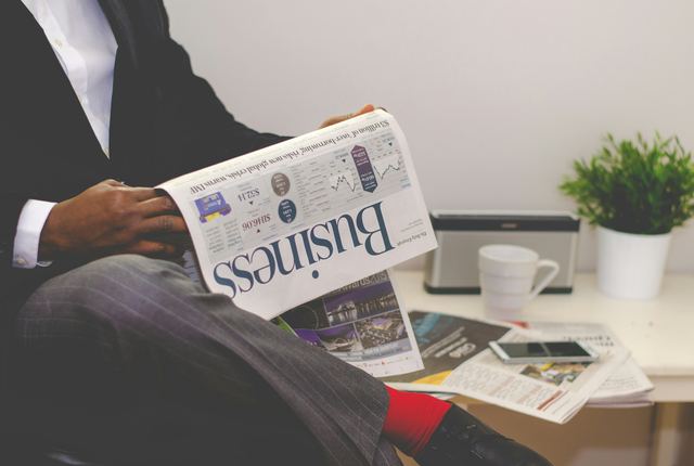 Pessoa sentada perto de uma mesa segurando um jornal de negócios aberto, acompanhando o mercado