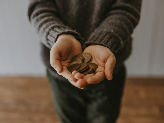 Criança segurando moedas de troco nas mãos, a mesada do mês