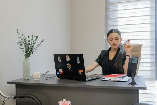 Mulher trabalhando à mesa com notebook e celular, acompanhando as vendas do mês