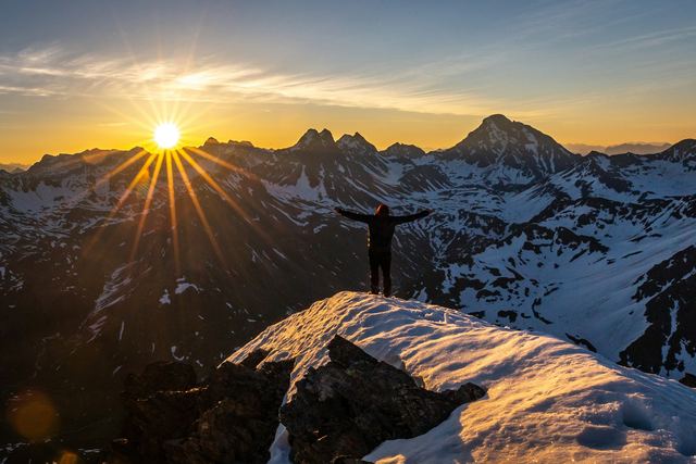 Pessoa em pé sobre um penhasco recebendo os primeiros raios de sol da manhã