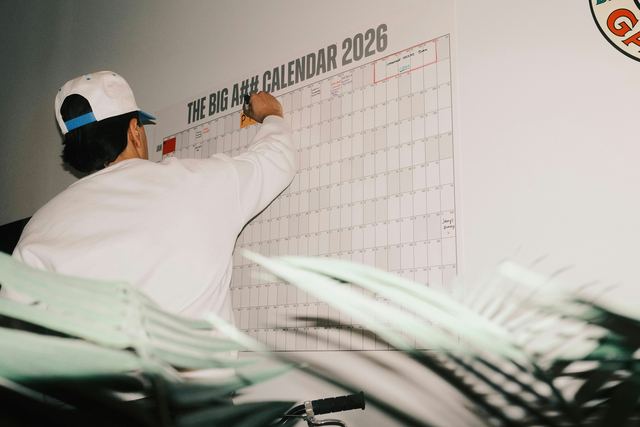 Homem escrevendo em um grande calendário de parede de 2026