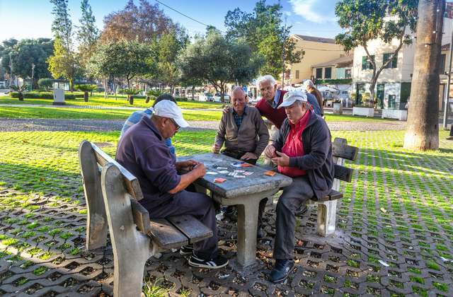 Homens idosos jogando cartas em uma mesa de parque.