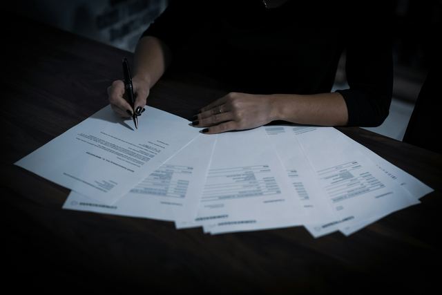 Mulher sentada à mesa assinando um documento entre vários papéis