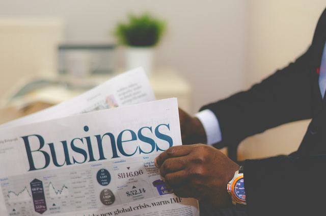 Homem de terno abrindo e lendo um jornal de economia, conferindo o noticiário de investimentos