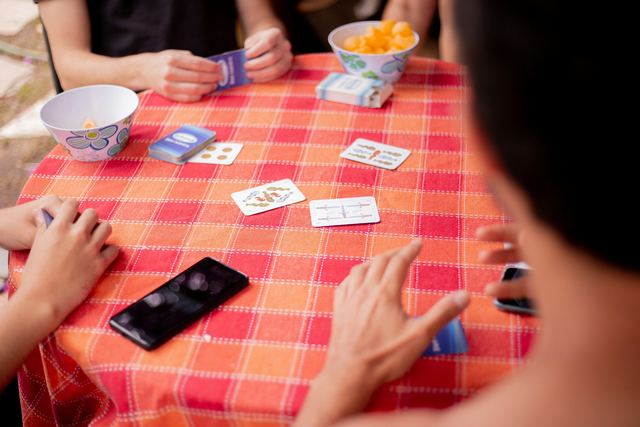 Pessoa segurando cartas de baralho sobre uma mesa durante uma partida entre amigos