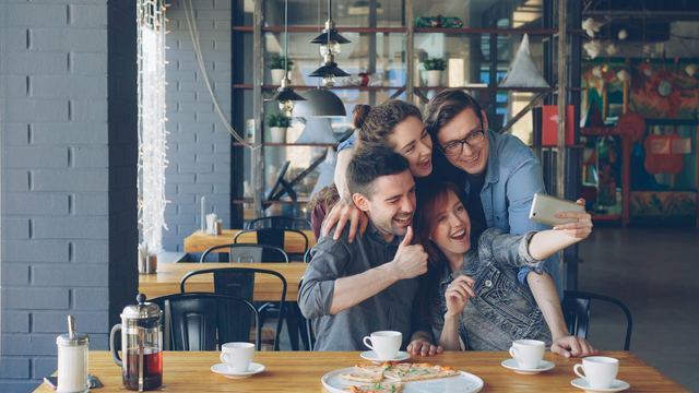 Amigos rindo e fazendo uma selfie juntos em volta de uma mesa de café