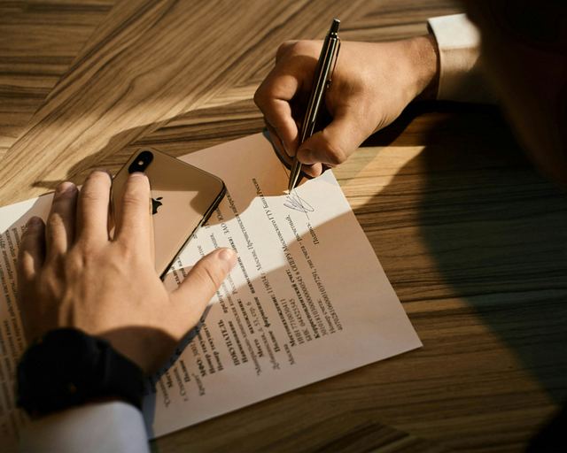 Mão de uma pessoa assinando um papel com caneta, em close, durante a assinatura de um documento