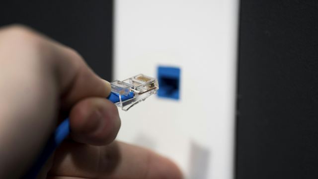 Mão de uma pessoa encaixando um cabo de rede azul e branco