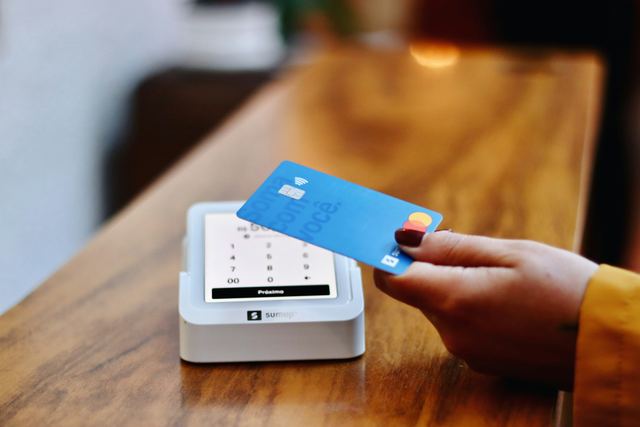 Pessoa aproximando um cartão de crédito da maquininha para pagar uma compra
