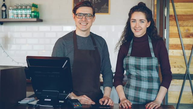 Dois atendentes sorrindo atrás do balcão de uma cafeteria moderna