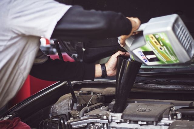Mecânico colocando óleo de motor no compartimento do motor de um carro