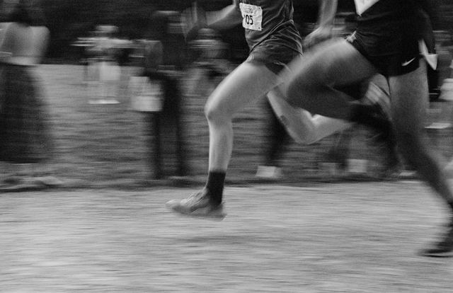 Dois corredores correndo lado a lado em uma prova de cross country, em preto e branco.