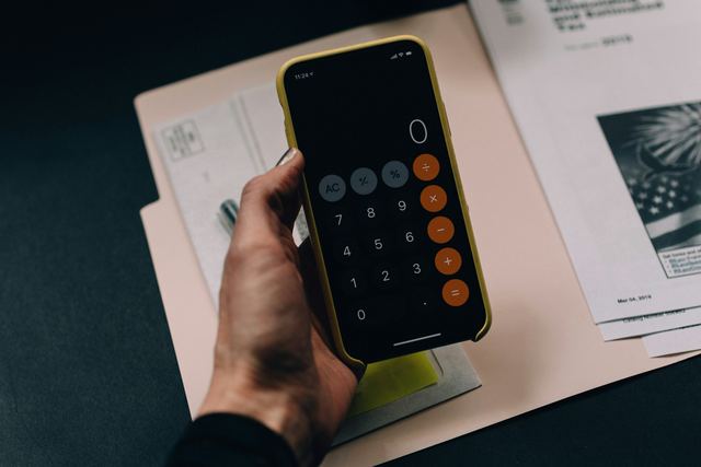 Mão segurando um celular com o aplicativo de calculadora aberto sobre uma pasta de papéis