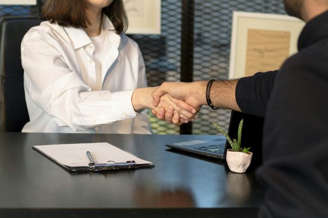 Um homem e uma mulher apertando as mãos diante de um notebook numa entrevista de emprego