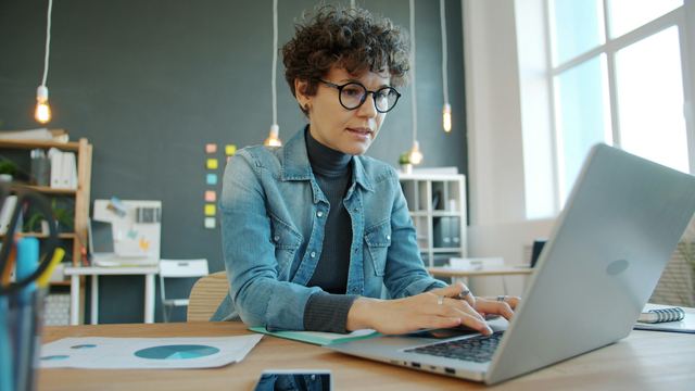 Mulher concentrada digitando no notebook, sentada a uma mesa de escritório moderno