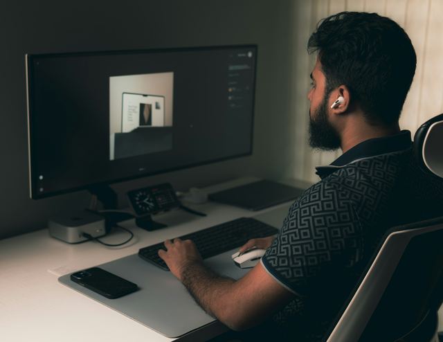 Homem de barba e fone de ouvido sem fio, visto de lado, analisa um layout de site em um monitor grande.