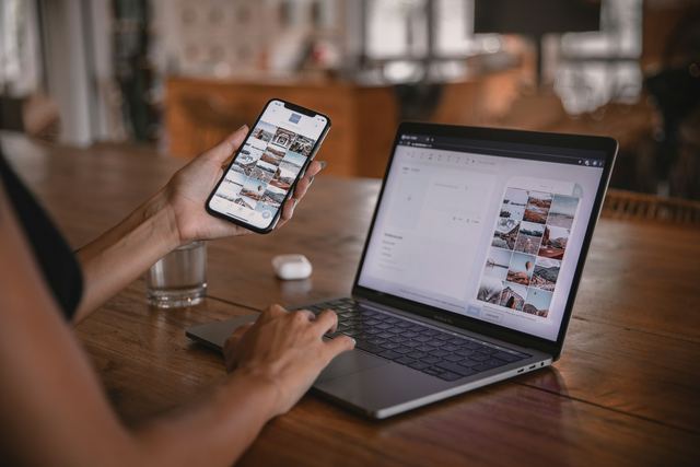 Mulher sentada à mesa com um notebook e um celular na mão conferindo o site