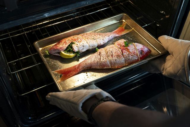 Pessoa tirando uma assadeira com peixe de dentro do forno