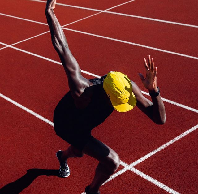 Velocista de boné amarelo arrancando para a largada numa pista de atletismo vermelha, vista de cima