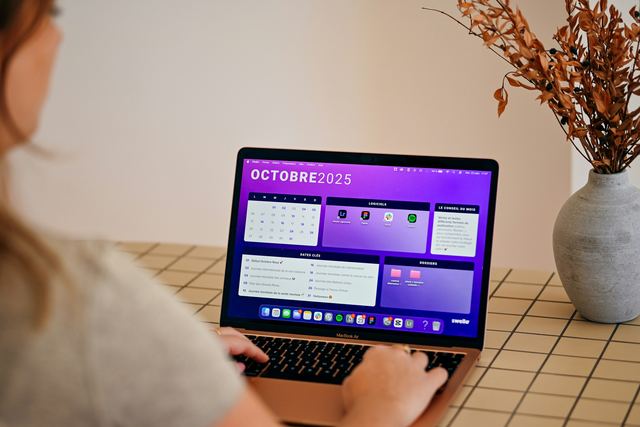 Mulher de costas usando um notebook que exibe um calendário do mês na tela, sobre uma mesa de madeira.