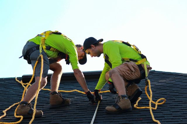 Dois instaladores de camiseta verde-limão e cinto de segurança medindo o telhado para colocar placas solares