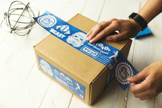 Mãos fechando com fita uma caixa de papelão de um pedido sobre a mesa