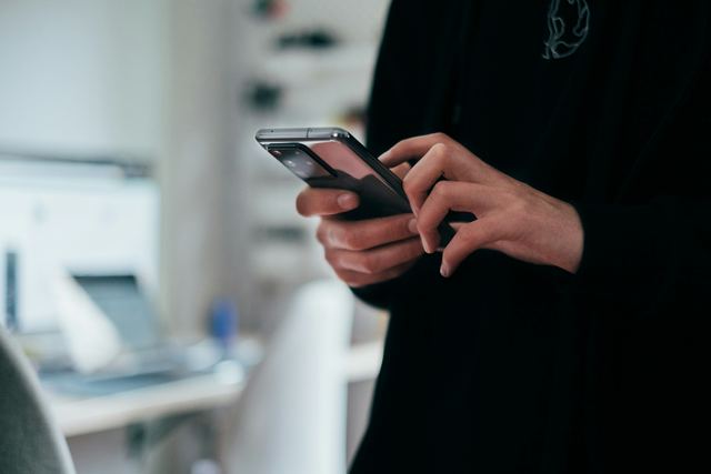 Jovem segurando um celular com as duas mãos para escrever uma mensagem