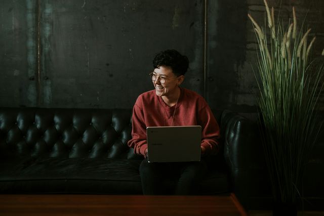 Homem sorrindo usando um notebook sentado num sofá de couro preto