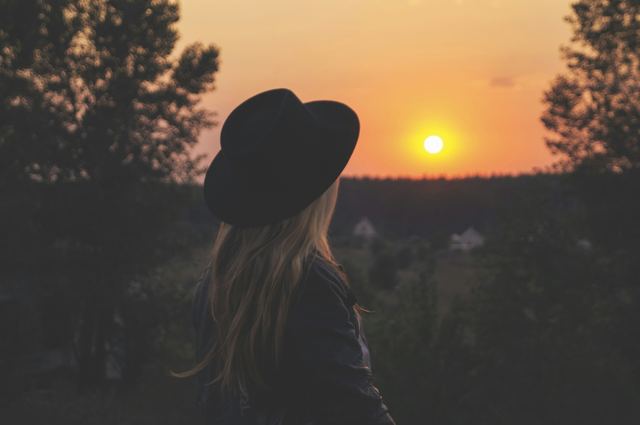 Mulher de chapéu preto olhando o pôr do sol.