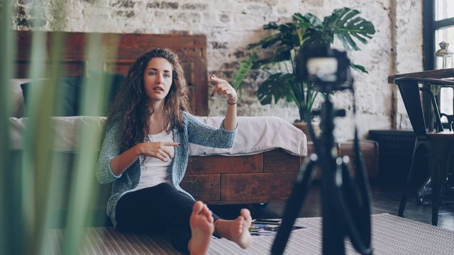 Jovem gravando vídeo sentada no chão de casa, com a câmera no tripé