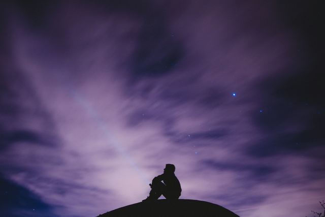 Pessoa sentada olhando para o céu estrelado à noite.
