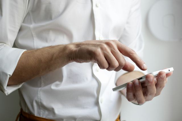 Pessoa de camisa branca segurando um celular com as duas mãos.