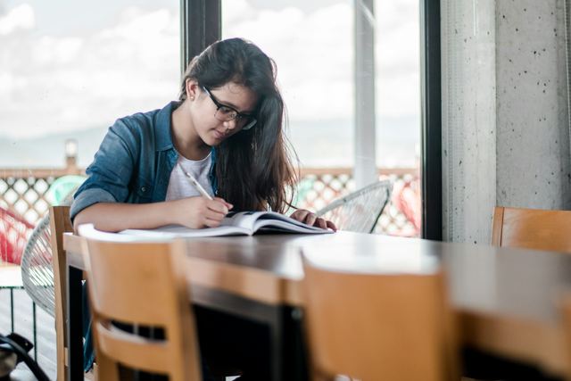Mulher escrevendo em um caderno aberto sobre a mesa