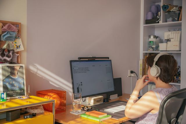 Pessoa de fones de ouvido sentada diante do computador em um escritório em casa