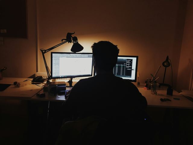 Homem diante do computador num quarto, trabalhando com código