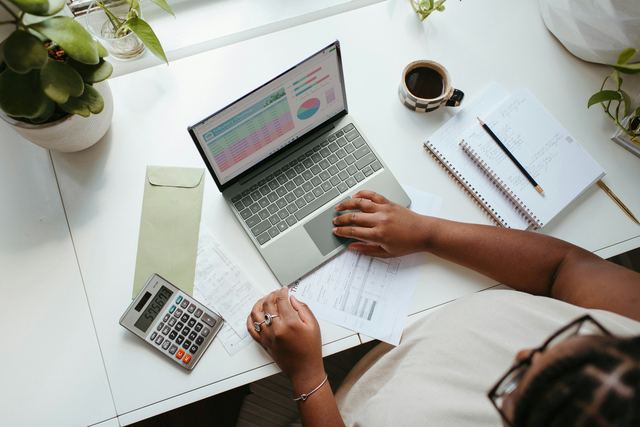 Pessoa sentada a uma mesa diante de um notebook, fazendo as contas do negócio