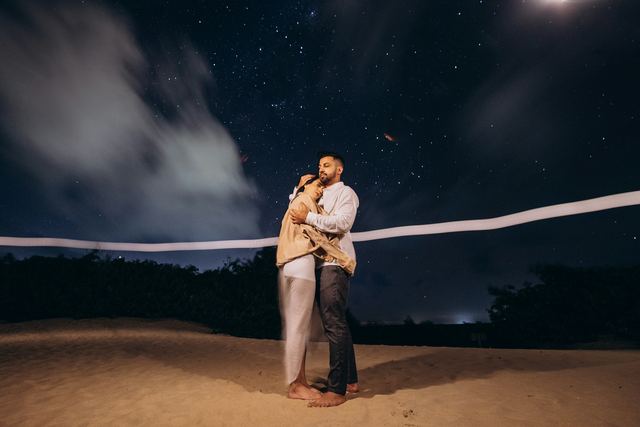 Casal abraçado na areia sob um céu cheio de estrelas