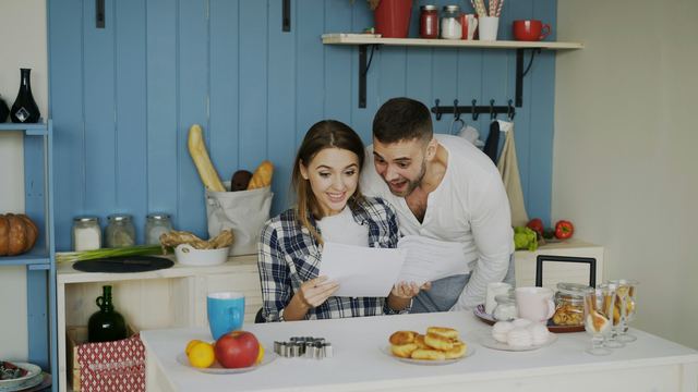 Casal sorridente lendo papéis juntos na mesa da cozinha, no café da manhã